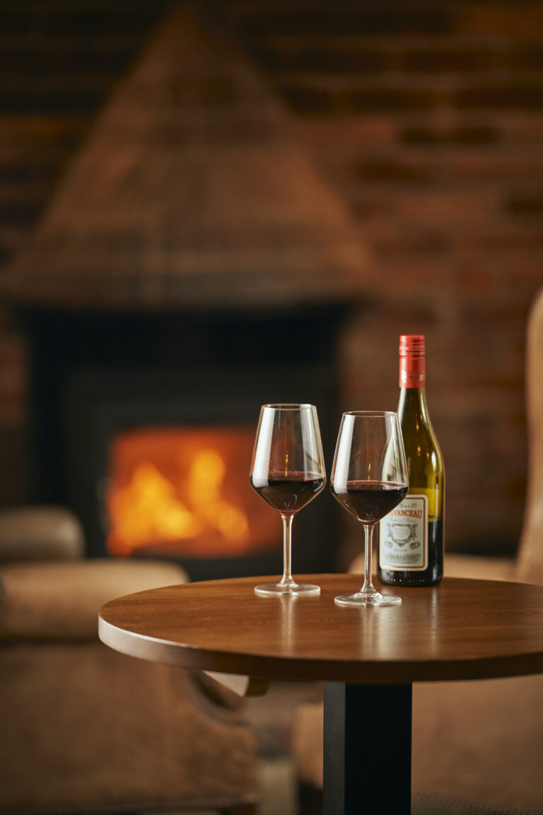 Two glasses and a bottle of wine infront of a fireplace at The Kingfisher