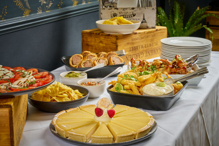 A table of food laid out including lemon tart and sausage rolls